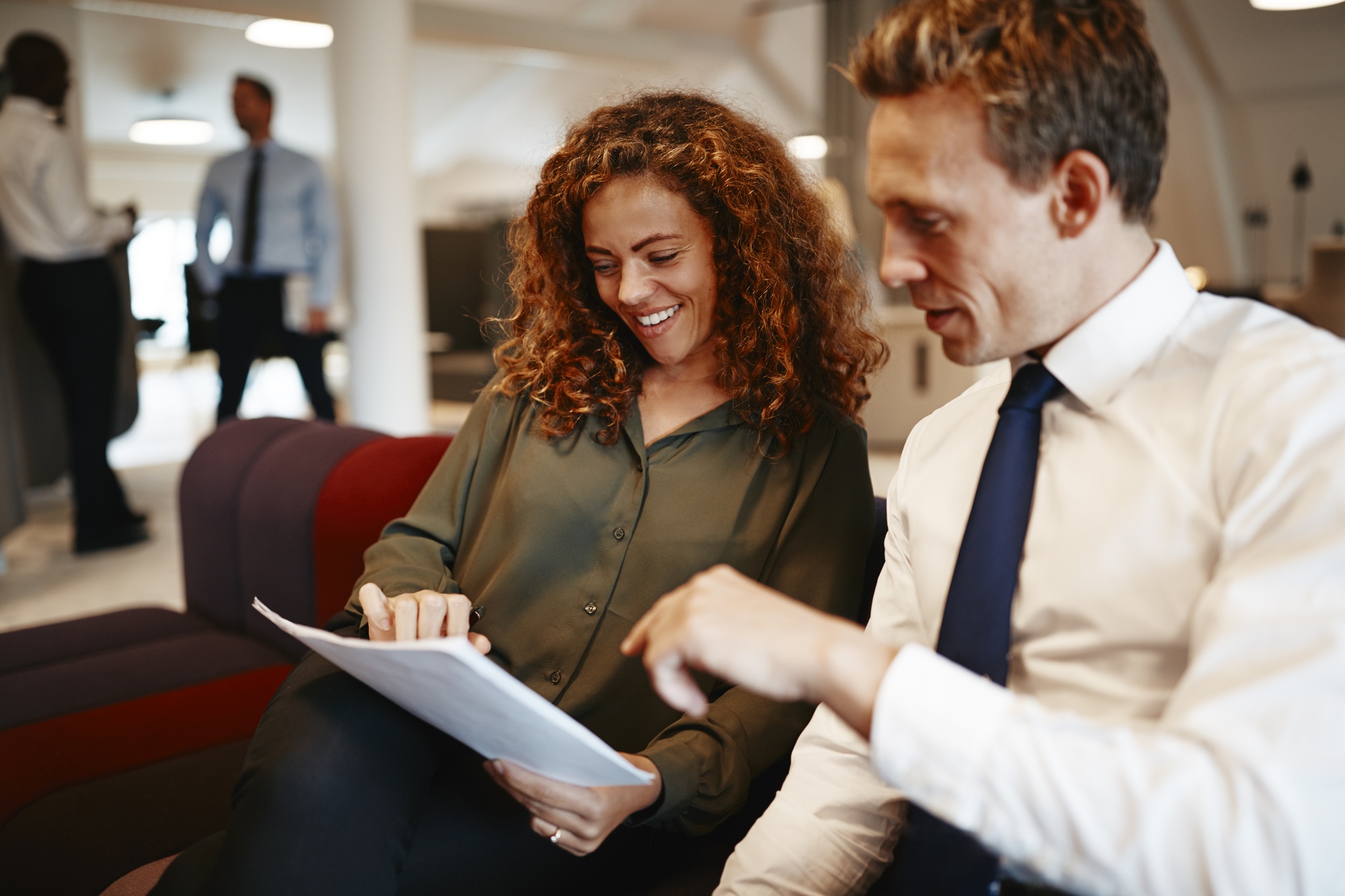 Smiling work colleagues discussing paperwork together on an office sofa